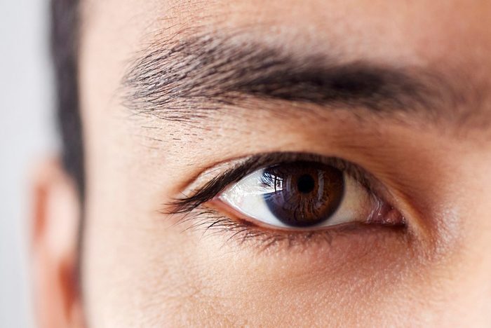 Closeup Portrait Of A Handsome Young Mixed Race Man Standing At Work In An Office Job. Young Hispanic Male With Naturally Long Eyelashes And Neat Eyebrows Showing His Healthy Brown Eye