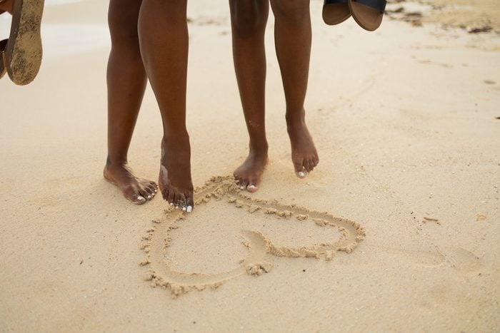 couple walking on the beach and drawing a Heart in the sand with their feet
