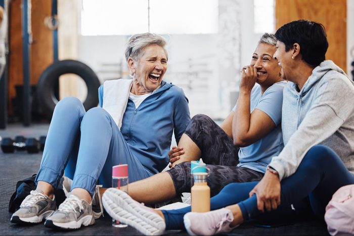 Gym, laughing and group of mature women telling joke after fitness class, conversation and comedy on floor. Exercise, bonding and happy senior woman with friends sitting chatting together at workout.