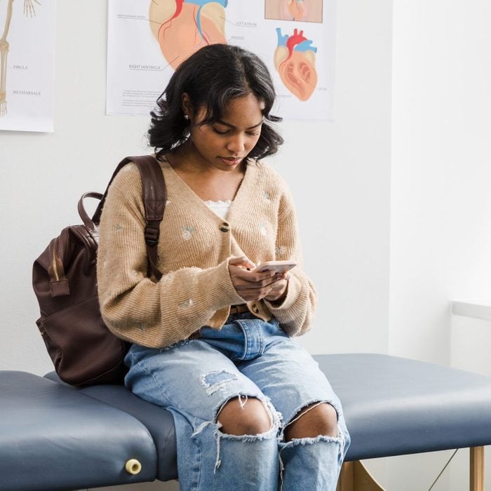 Teen girl uses smart phone while waiting for doctor