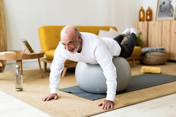 Active senior man exercising on fitness ball at home 