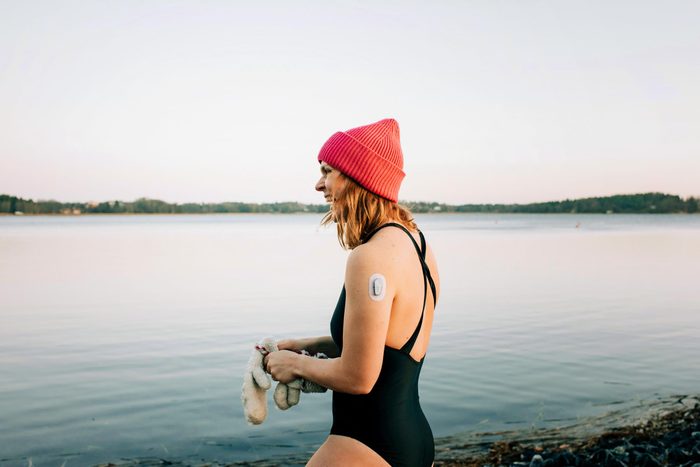 woman about to cold plunge int oa lake wearing a red hat and holding mittens