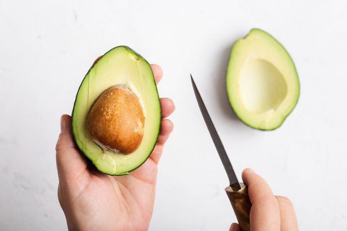 Cropped hands of woman holding halved avocado and knife