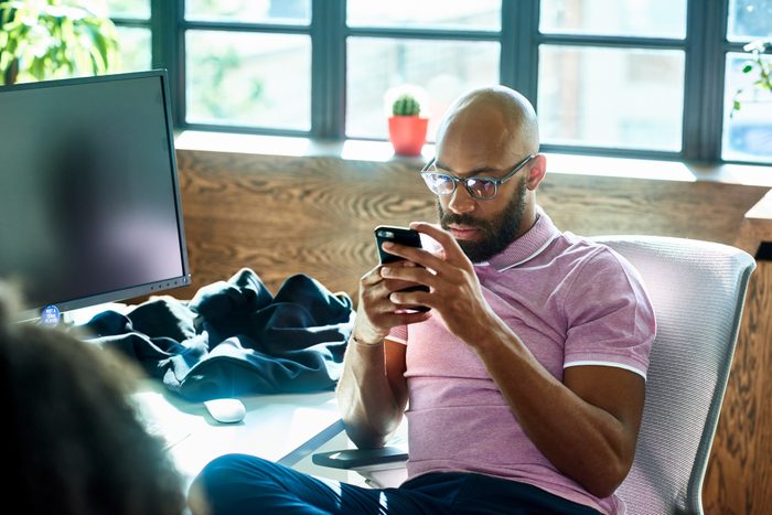 Mid adult man with beard and glasses texting in office