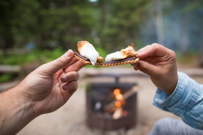 Couple toasting with their s'mores over campfire.
