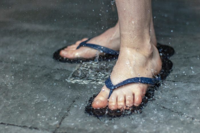 Flip flops on the feet of a person washing in the shower. Close up.
