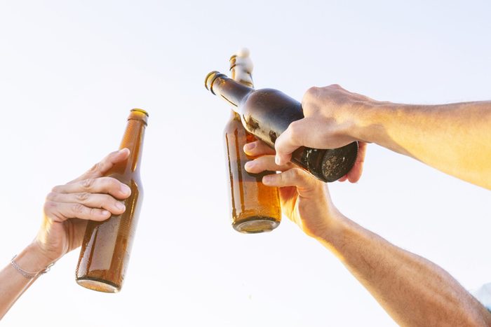 Three people doing celebratory toast with beer bottles on beach at sunset, Oliva, Valencia, Spain. - stock photo