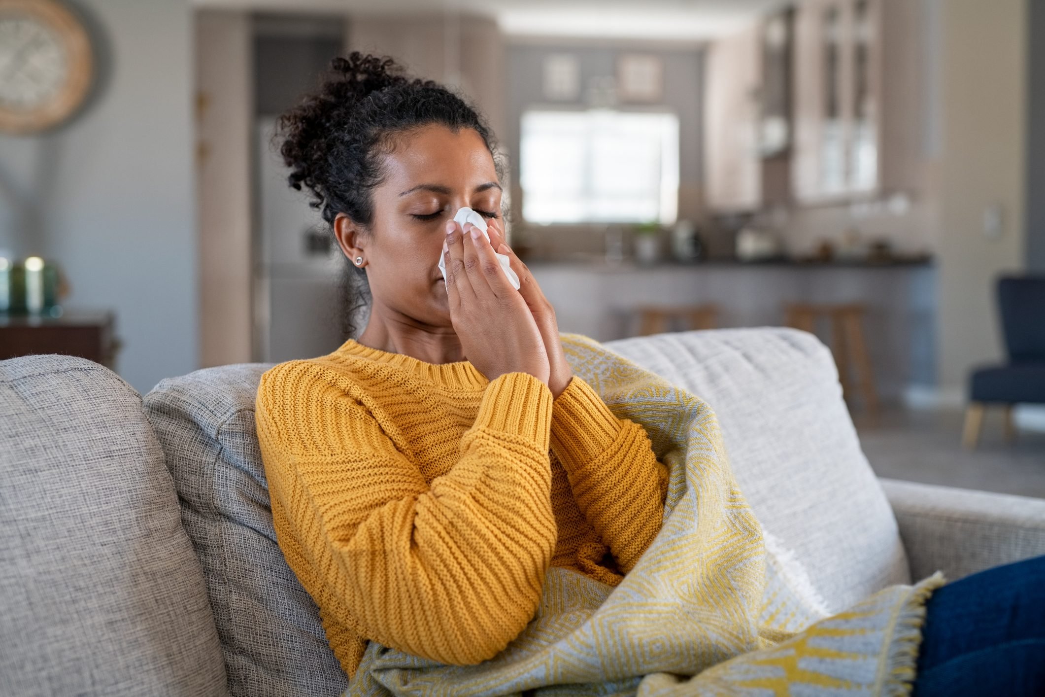 woman sitting on couch at home sick with cold or flu|bowl of chicken soup for common cold