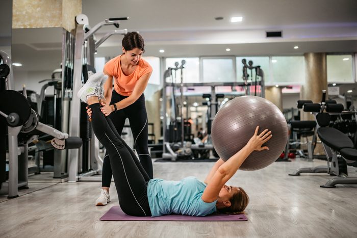 Senior woman training in gym with trainers help