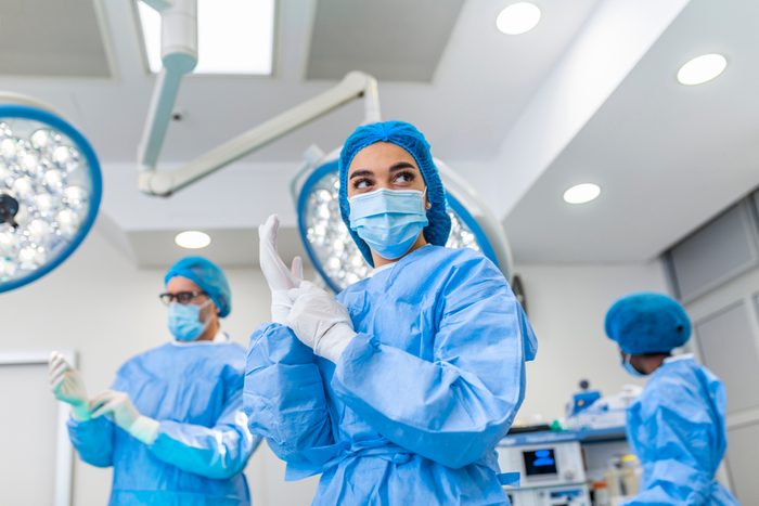 Portrait of female surgeon in surgical uniform in operation theater looking away. Doctor in scrubs and medical mask in modern hospital operating room.