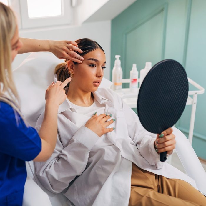 Dermatologist prepares the patient for facial treatment while she looks herself in the mirror