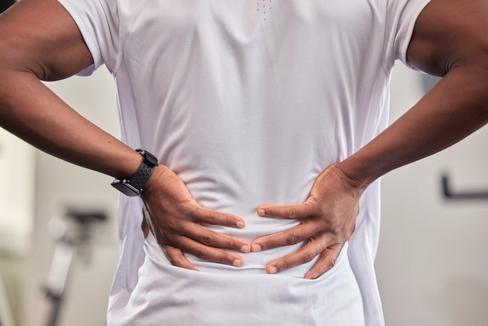 Back pain, hands and fitness injury in gym after accident, workout or training. Sports, health and black man or athlete with fibromyalgia, inflammation or arthritis, tendinitis or painful fracture.