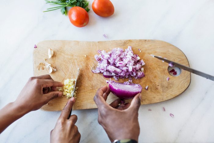 Cropped image of couple cutting onion and garlic on cutting board in kitchen