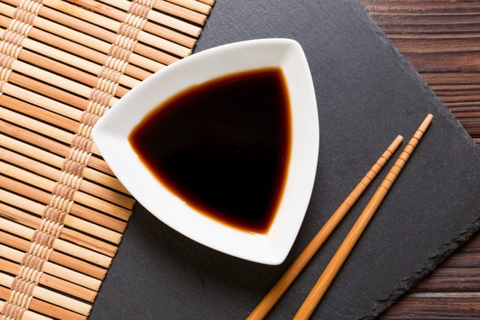 Chopsticks and soy sauce on black stone plate, wooden background with copy space