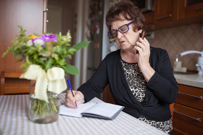 Senior woman talking on phone and and writing in her home
