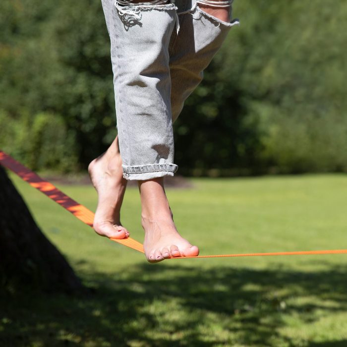 A person walking on slackline training balance with bear foot on a warm sunny summer day in a green garden. Healthy living concept.