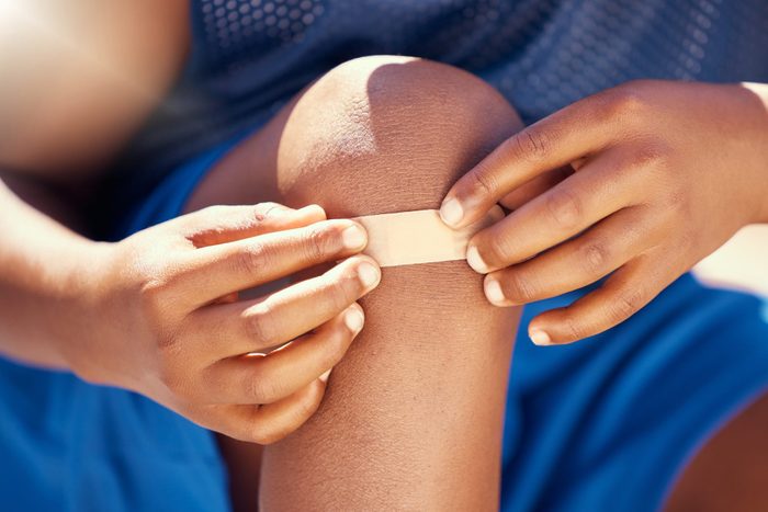Children, accident and plaster with a band aid on the knee of boy with an injury, wound or pain. Kids, cut and heal with the hands of a male child outside with a scrape, bruise or injured anatomy
