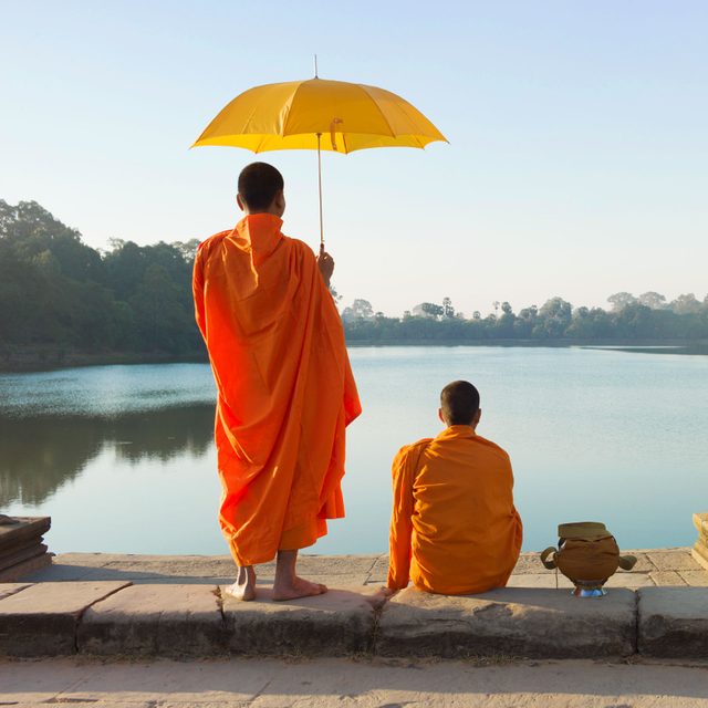 two monks looking at the water, one holding a yellow umbrella