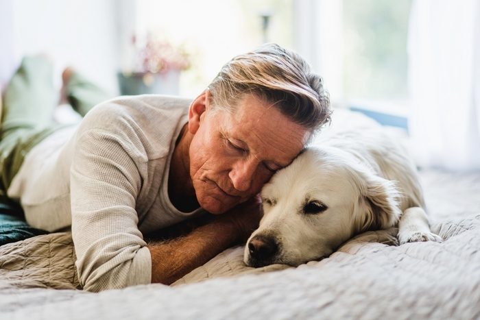 man hugging his old golden retriever dog on a bed