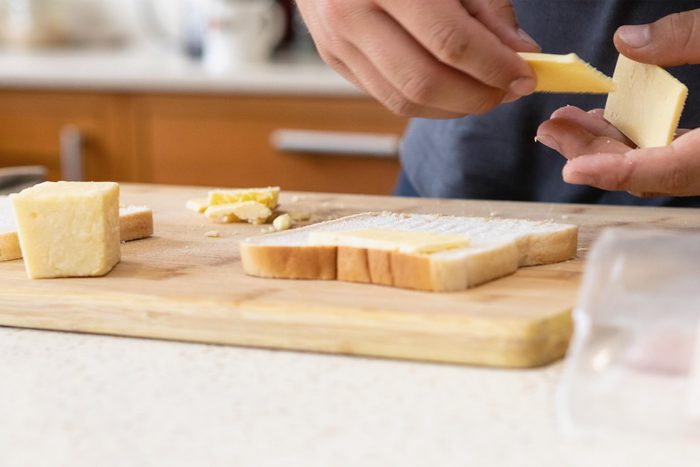 Teenage hands placing slices of cheese on white bread on a board