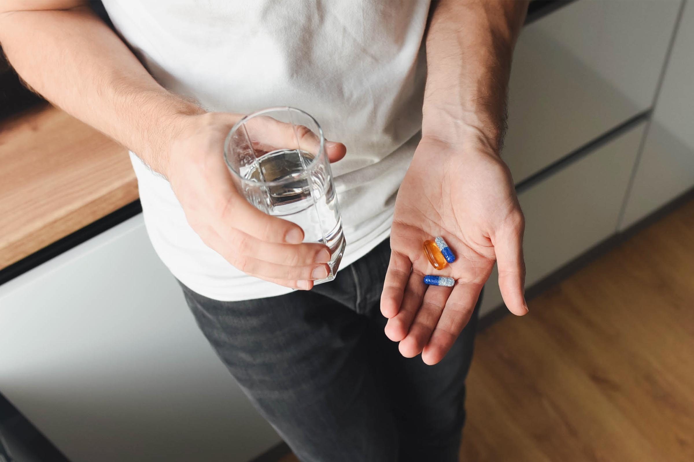 Man holds vitamins and pills in his hand in the kitchen