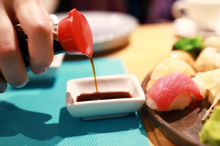 hand pouring soy sauce into a small white dish at a sushi restaurant
