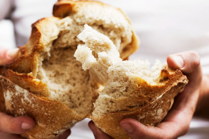 hands breaking loaf of bread in half
