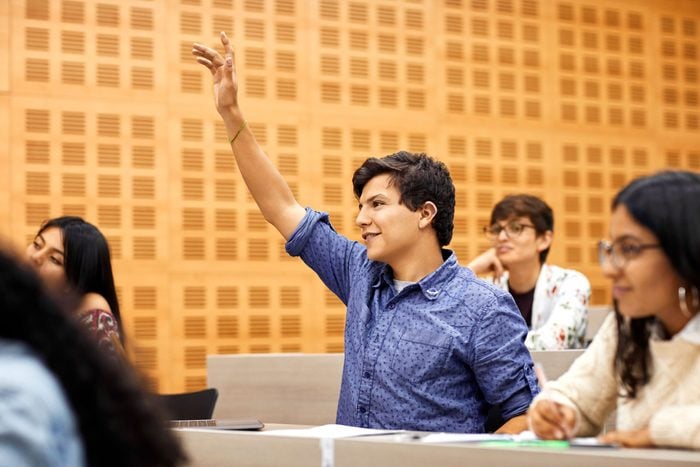 Smiling student with hand raised in lecture hall