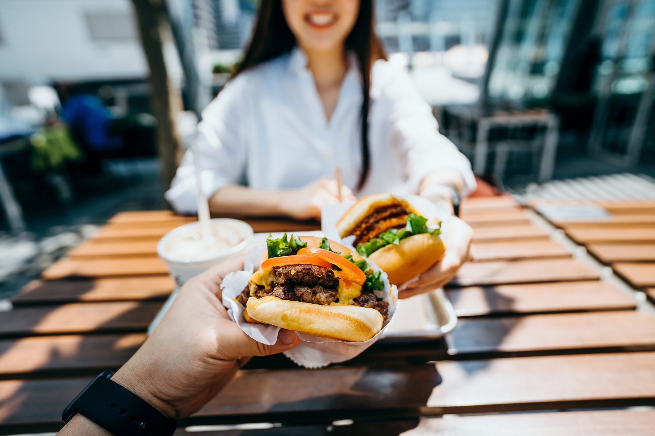 Happy young Asian couple eating beef burger with fries in an outdoor fast food restaurant