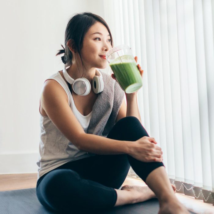 woman drinking green smoothie while doing yoga