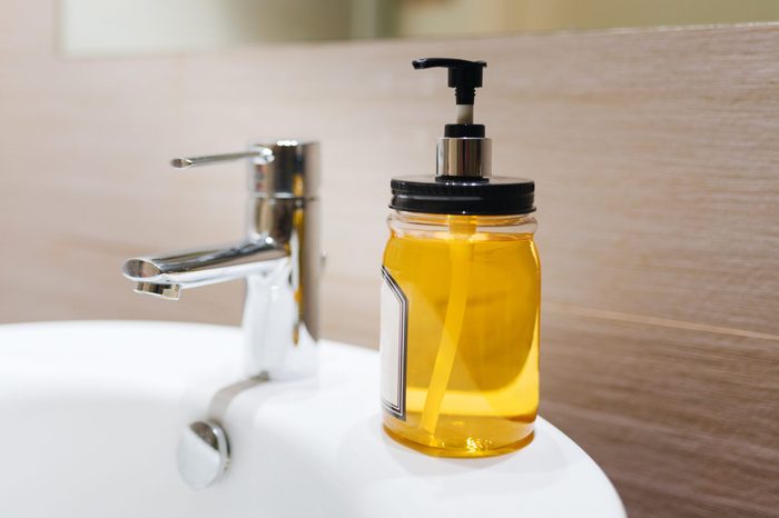 Close-up view of a bottle of yellow hand soap next to a bathroom faucet. Organic hand sanitiser