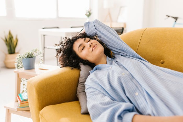 Smiling young woman with eyes closed resting on sofa and thinking about food