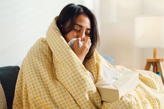 woman under a blanket with tissues sick with either the flu or covid