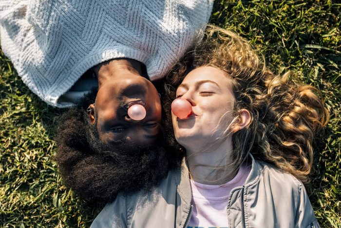 Two best friends making a gum bubble lying in the grass