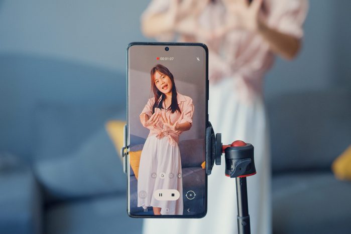 Happy young Asian girl blogger front of phone camera record video enjoy with dance content in living room at home. Social distance coronavirus pandemic concept. Freedom and active lifestyle concept