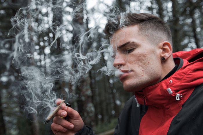 Young Man Smoking weed Standing In Forest During late Autumn