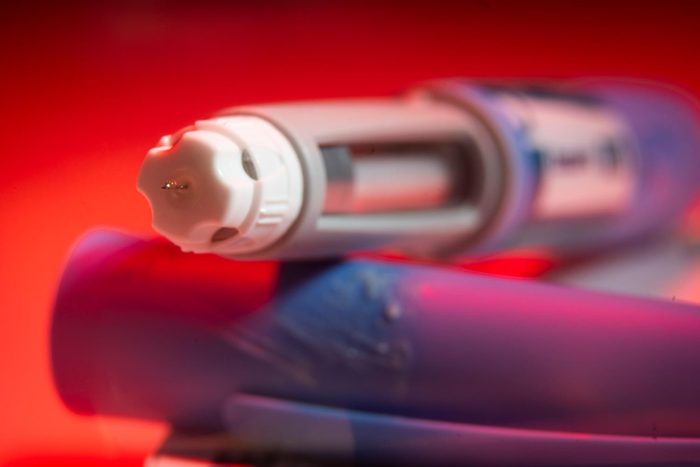 An Uncapped Ozempic Needle of an injection pen is pictured on a bright red background