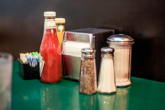 A Table at a Cafe Diner With Tomato Ketchup, Mustard, Salt and Pepper, Napkins and Parmesan Cheese on a Bright Green tabletop