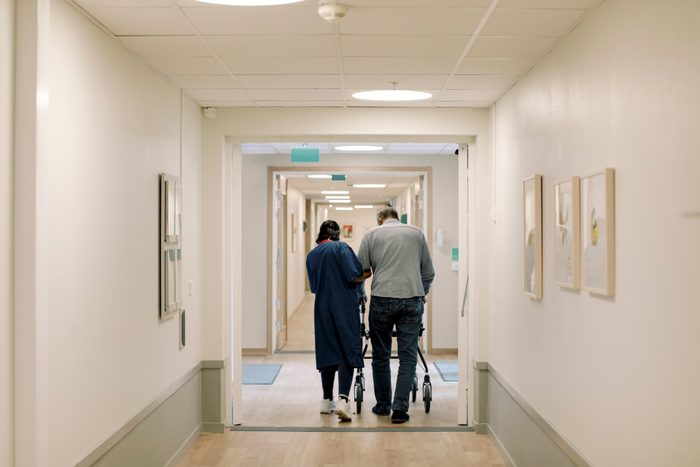 Rear view of female nurse walking with senior man in corridor at nursing home