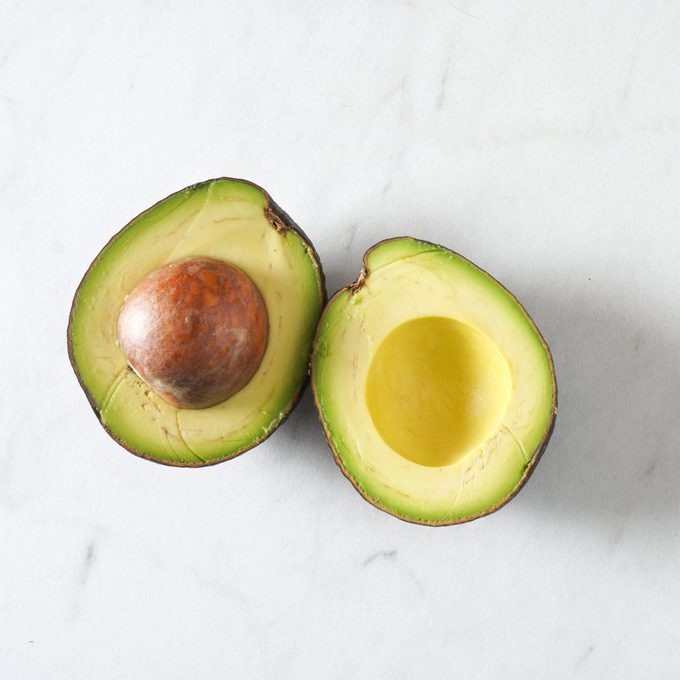 Two avocado halves rest on a white marble countertop with copy space