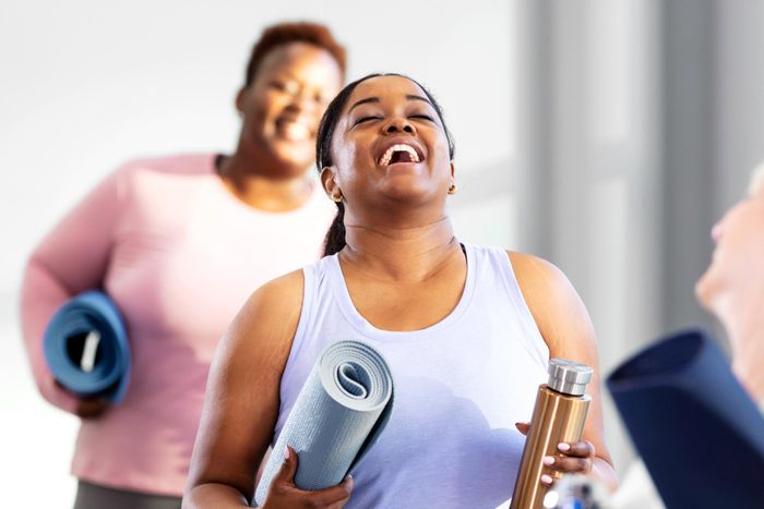 Three multi-ethnic women arriving at exercise class laughing holding yoga mats