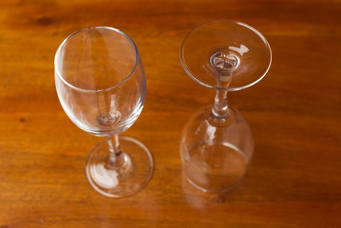 two empty wine glasses on wood surface; one glass is upright, the other is upside down