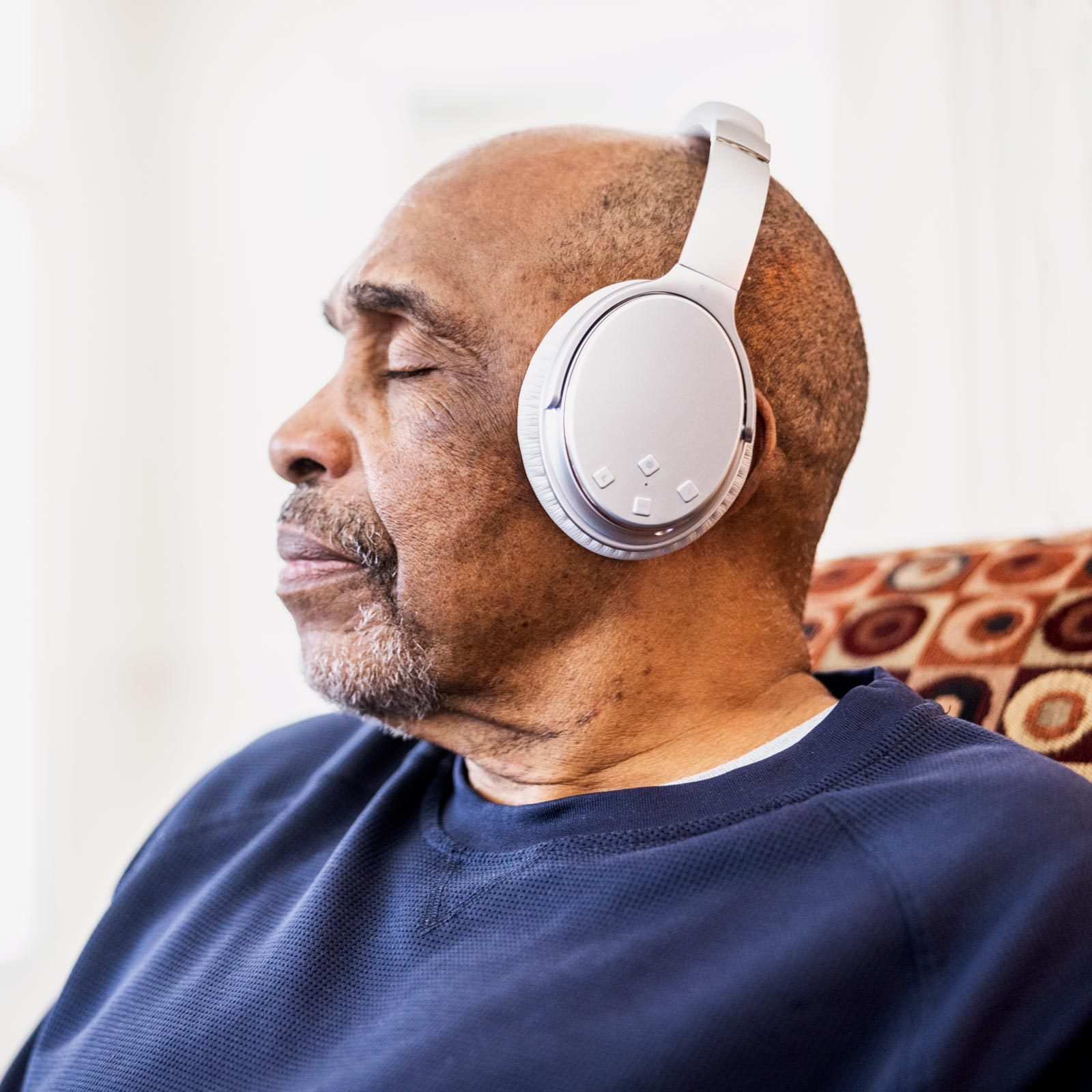 Senior man listening to music on wireless headphones at home