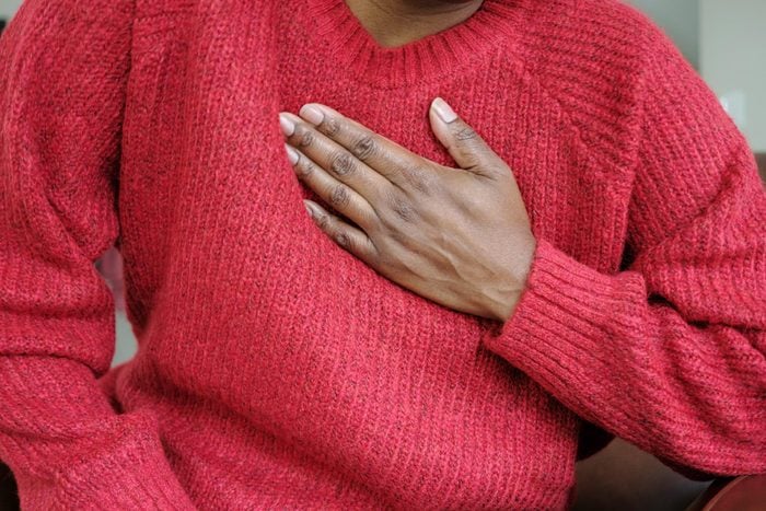 woman holding her chest experiencing a heart attack wearing a red sweater in december