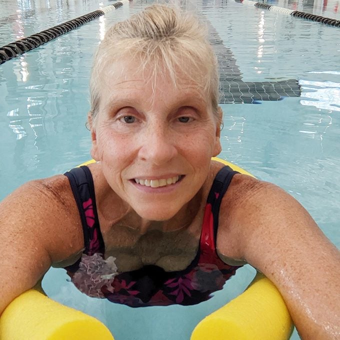 woman in a pool smiling with a yellow pool noodle
