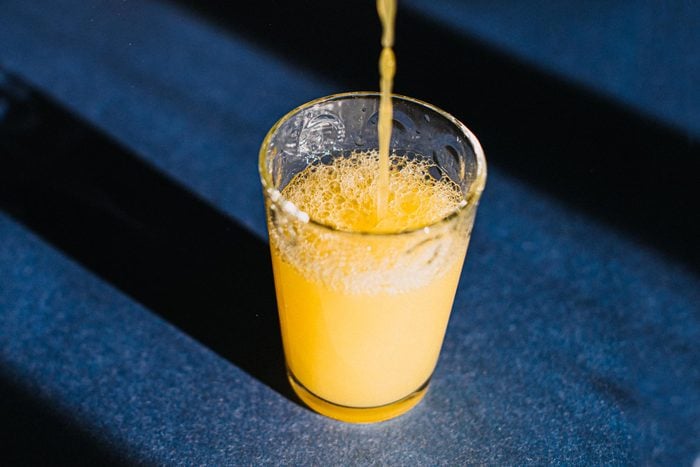 ginger shot being poured into glass on a blue background