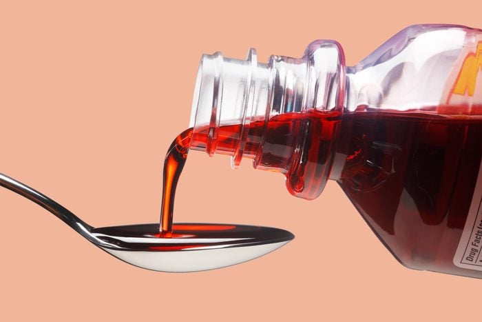 cough syrup being poured onto a spoon, on a light orange background