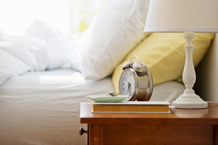 alarm clock and lamp on a bedside table next to a bed with white and yellow pillows