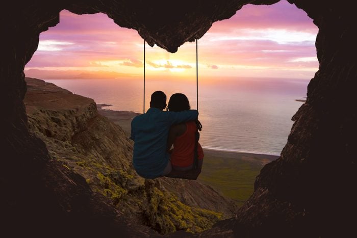couple sitting on a swing surrounded by a silhouette of a rock formation in a shape of heart