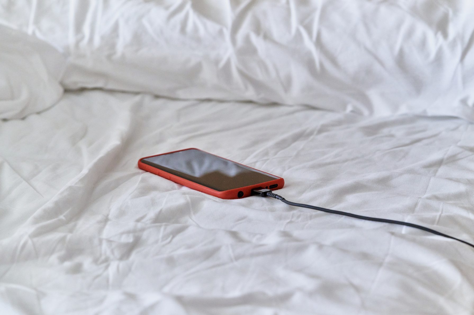 cell phone left charging on a bed of pillows and white blanket in the bedroom with the able facing the wall